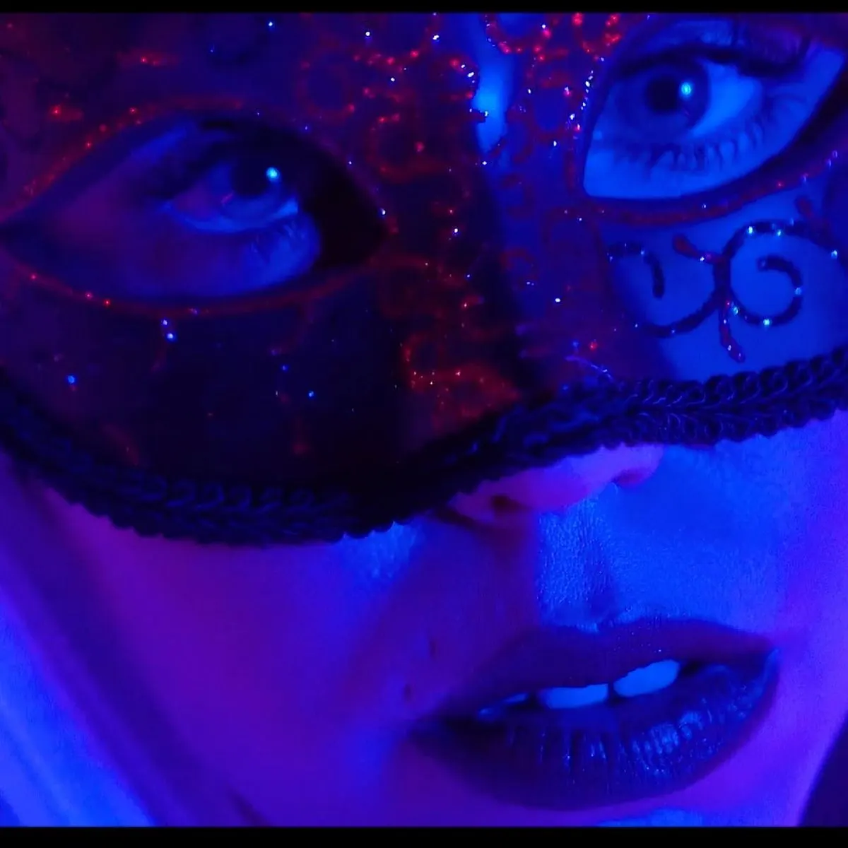 Close-up of a face in a masquerade mask under blue light