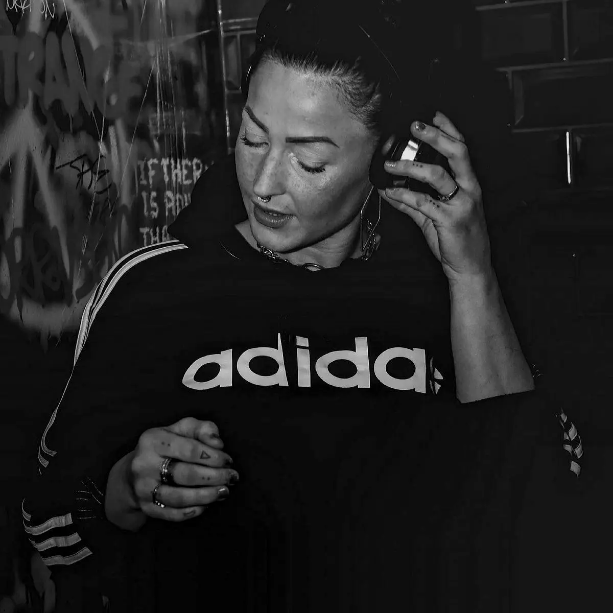 Woman DJ listening on headphones in front of graffiti