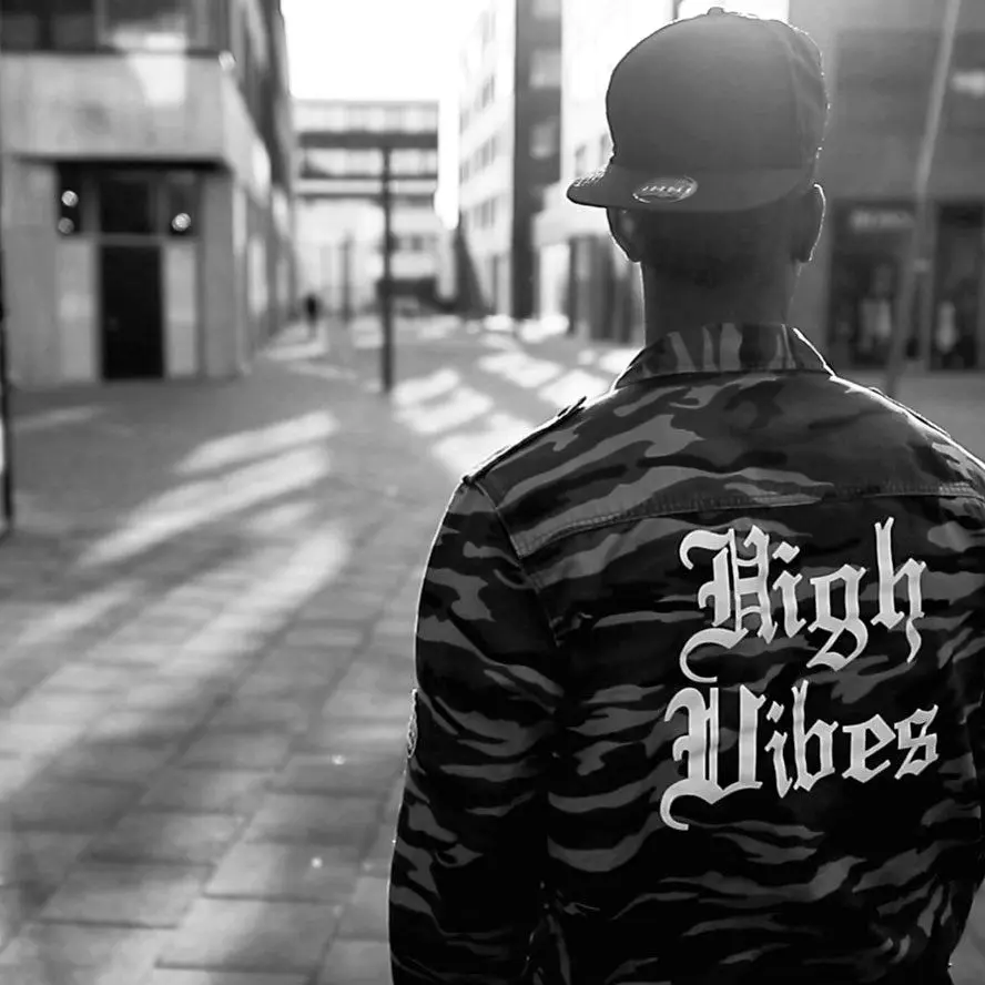 Back of a camouflage jacket printed High Vibes on an empty street