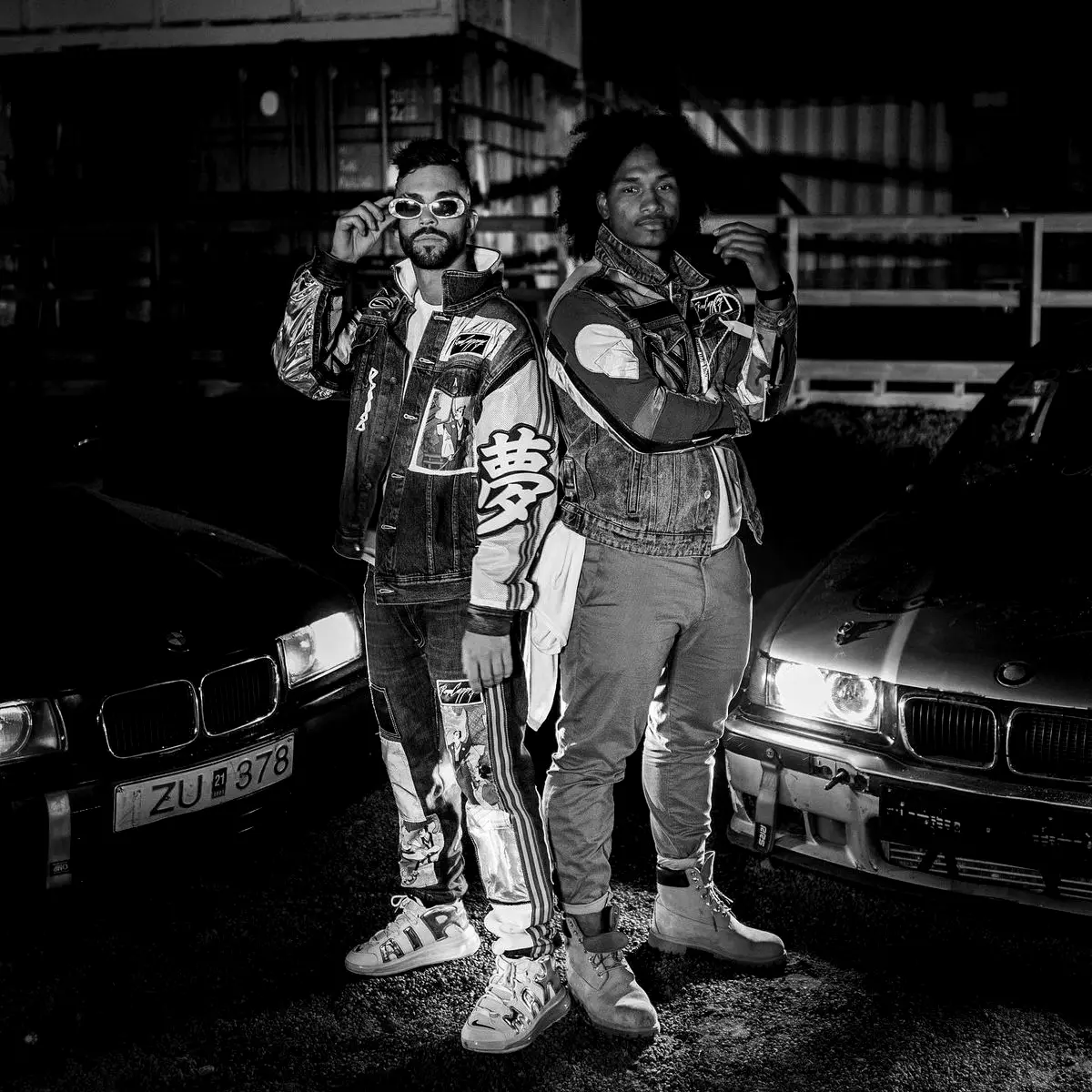Two artists posing beside parked cars at night