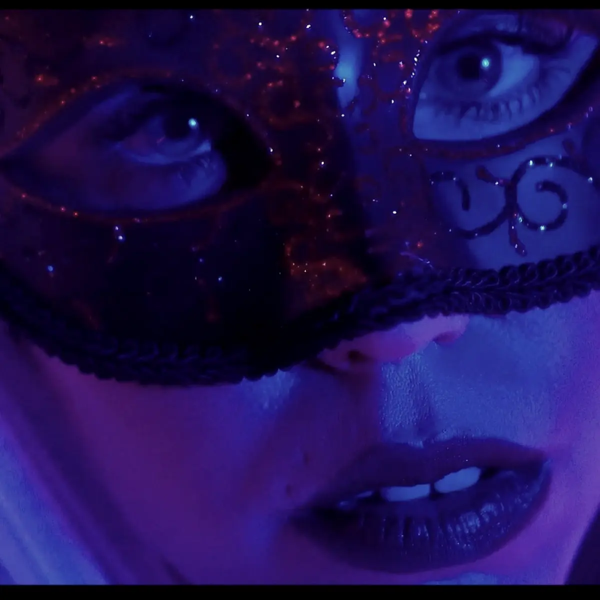 Close-up of a face in a masquerade mask under blue light
