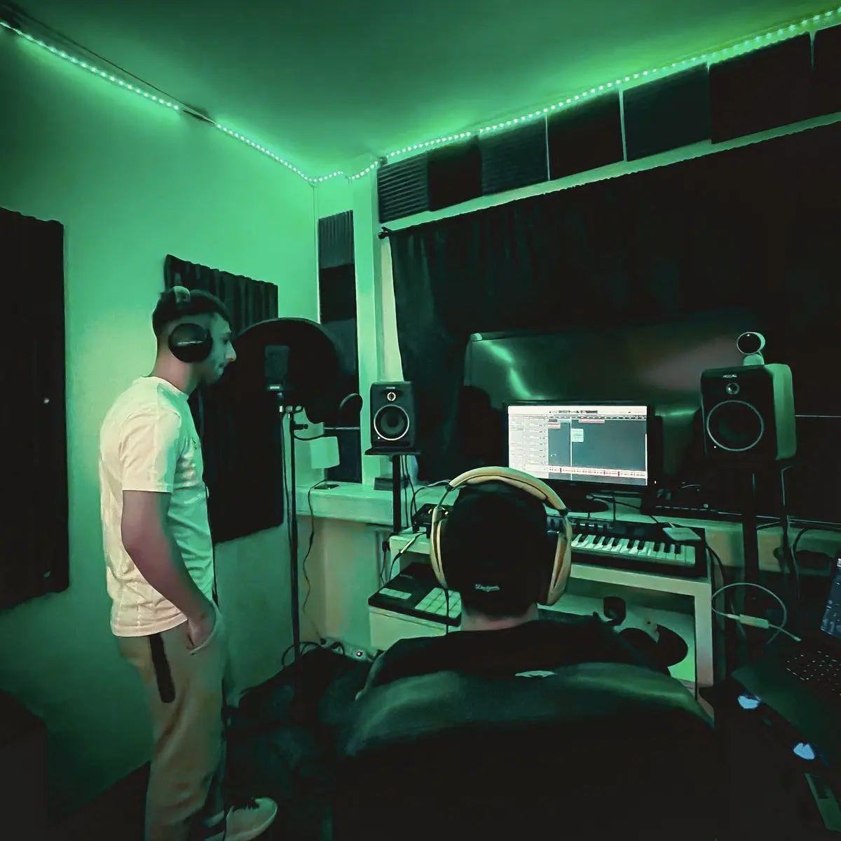 Two people working in a green-lit recording studio