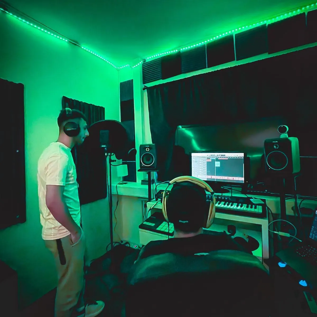 Two people working in a green-lit recording studio